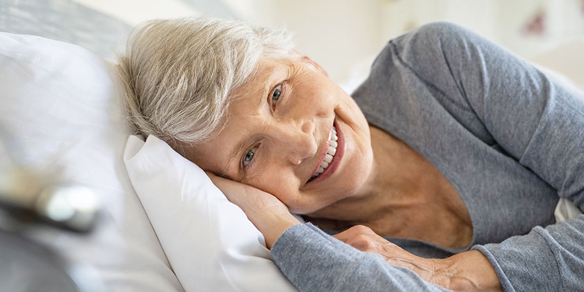 anziana allettata sorridente con cuscini per posizionamento a letto